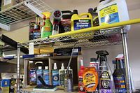 Two metal shelves filled with various car care cleaning and maintenance products, including spray bottles, jugs, and tools like a telescoping squeegee and vintage oil can.