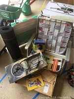 Three folding lawn chairs, compact electric burner and broiler on the ground, yoga mat rolled up, gardening supplies in background.