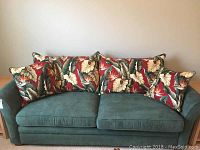 Full view of green fabric sofa bed with six floral print accent pillows arranged on the backrest.