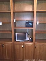Full view of wooden book shelf showing four open shelves and two-door cabinet, with TV and electronics placed on shelves for scale.