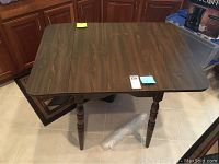 Full view of wooden drop leaf kitchen table with turned legs on tiled floor.