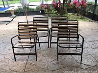 Four brown metal frame patio chairs with tan webbing seats and backs arranged on patio floor