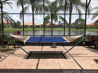 Full view of the hammock set up on a patio with screened enclosure, showing the green metal frame and blue polka dot canvas hammock suspended.