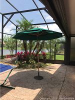 Full view of the large green outdoor umbrella open with metal base and wooden frame in a screened patio.