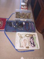 Wide overhead shot showing three containers filled with assorted jewelry items: multiple necklaces, earrings, and brooches in various designs.