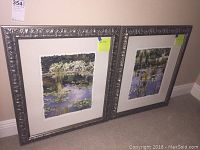 Two framed impressionistic garden and pond paintings with ornate dark carved frames and white mats, positioned side by side on floor.