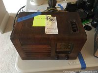Side and angled view of a vintage wooden General Electric radio placed on a table showing its slatted speaker grille and control knobs with taped note.