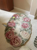 Top-down photo of oval wool rug with large roses pattern in rose, cream, green colors. Shows overall shape and design.