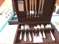 Reed & Barton flatware set displayed in open chest showing knives, forks, and spoons.