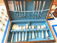 Open wooden box showing 50-piece WM Rodgers silver flatware set housed in blue felt lining with elastic securing bands.