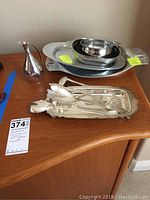 Silver-plated pitcher, oval serving platters, nested serving bowls, and five pieces of flatware on a wooden surface.