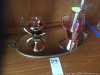 Overall photo showing the oval mirror tray with gold trim along with the rose-colored glass decanter and round container placed on it.
