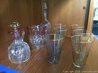 Front view of the glassware set showing decanters, tinted glasses, and vase on wooden shelf