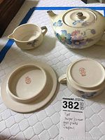 Photo showing the tea set pieces including teapot, sugar bowl, creamer, and hot plate with visible floral patterns and Japanese marks on the bottom.