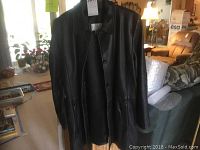 Front view of black leather women's jacket on hanger, showing full length and buttons.