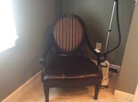 Front view of the dark stained wooden arm chair with leather seat and striped fabric upholstered backrest, positioned against a wall near carpeted floor.