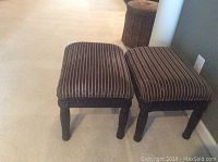Pair of dark striped fabric ottomans with carved dark wood legs on carpeted floor.
