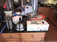 Overview of lot on kitchen countertop including kettle, stock pot, mixers, baking dishes, mandoline slicer in box and other items