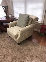 Front angled view of upholstered accent chair showing rolled arms, floral damask upholstery and green accent pillow.
