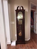 Full front view of the tall mahogany-finished longcase clock showing pediment, dial, weights and glass door.