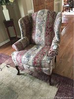 Front left angled view of the wingback chair showing the floral striped upholstery and wooden cabriole legs.