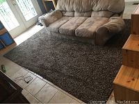 Brown textured rug under a beige couch on tiled floor.