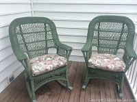 Two light green wicker rocking chairs with floral cushions on wooden deck.