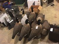 Eight decoys arranged on floor with bag and miscellaneous background items