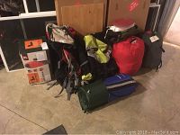 Photo showing multiple sleeping bags in storage sacks and several backpacks grouped on the floor.