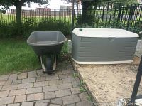 Wheelbarrow and storage bin placed outdoors on a paved area and grass.