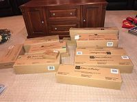 Several closed cardboard boxes labeled 'Home Interiors' arranged on carpeted floor in front of wooden furniture.