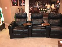 Front view of three black leather theater seats showing two seats with three armrests and two tray tables