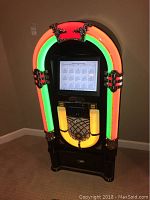 Front view of black Crosley jukebox with neon arch and touchscreen display powered on