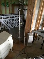 Full view of tall wrought iron easel standing on floor against wooden wall background.