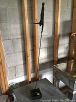 Side view of the wrought iron sculpture showing the figure balanced upside down on a slender rod fixed to a square base.