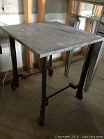 Front-side view of square tin tabletop on iron frame with caster wheels