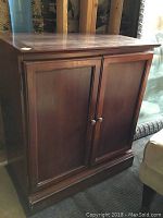 Front and side angled view of the brown wooden two-door cabinet showing paneled doors and metal round knobs.