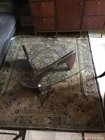 Carpet with a brown, black, beige, and muted floral design under a glass coffee table, showing overall pattern and wear.