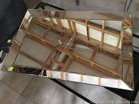 Rectangular beveled glass mirror lying flat on two chairs reflecting wooden ceiling beams.