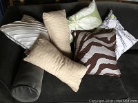 Six assorted decorative throw pillows arranged on a dark grey couch showing various patterns and textures.