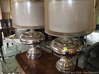 Two chrome table lamps with drum fabric shades on wooden surface