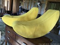 Front and top angle view of two yellow crescent moon shaped child's seats on wooden furniture against a workshop background.