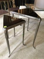 Oblique photo showing both triangular nesting tables with steel legs and black glass tops, one nested inside the other.