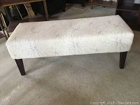 Front-side angle view showing the rectangular shape, floral upholstery on the cream fabric, and dark wood legs with subtle texture visible on the fabric surface.