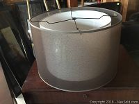 Side view of grey fabric lampshade on wooden surface showing exterior and shape.