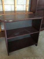 Front view of dark wooden shelf showing two open shelves and marks on the surfaces, placed in a storage setting.