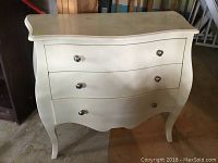 Front view of white dresser showing three curved drawers with metal knobs and some surface markings.