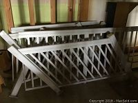 Stack of white metal fencing sections including straight and angled stair railing pieces leaning against wall