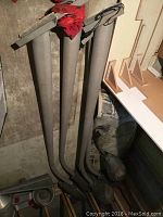 Five long metal poles with mounting hardware at top, appearing dusty and stored upright in a basement or shed area.