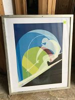 Framed modern skiing artwork showing a stylized skier in white against abstract blue, green, yellow circles and black slope.